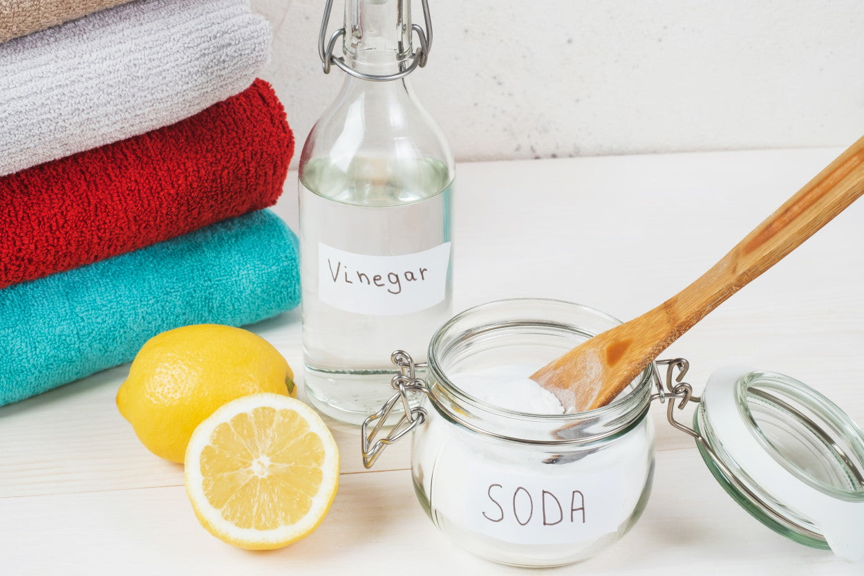 Containers of vinegar and baking soda next to cut lemon and stack of clean towels