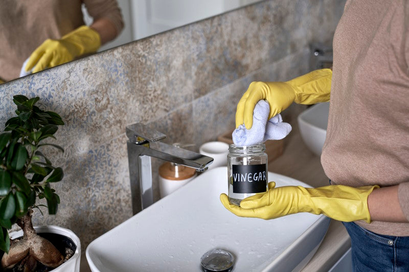 Person wearing rubber gloves and dipping a cleaning cloth into a bottle of vinegar