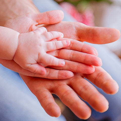 foto di mani che si sovrappongono, alla base quella di un padre in mezzo quella di una madre e in fine quelle del bebè