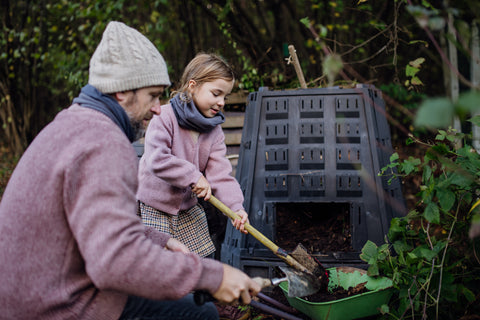 Girl helping father to remove compost from the composter in the garden. Concept of composting and sustainable organic gardening.