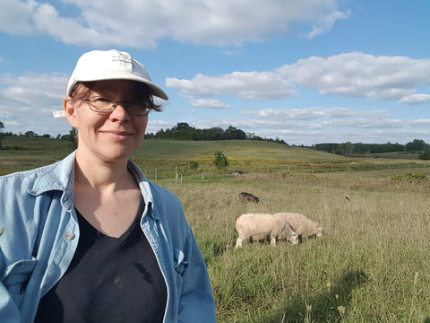 Jenn Osborn, owner of EcoWool, standing in a field with her sheep grazing behind her in the field.