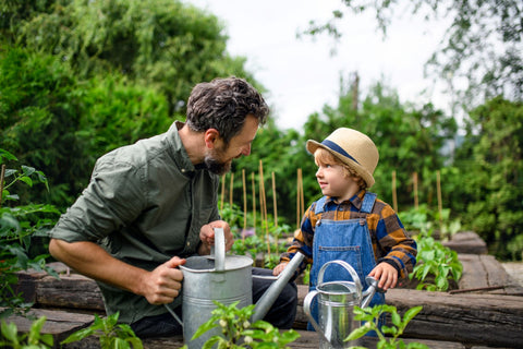 Caucasian man with child in garden with matching metal watering cans.