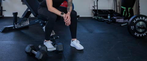 Someone sitting on a weight bench with Dumbbells at their feet