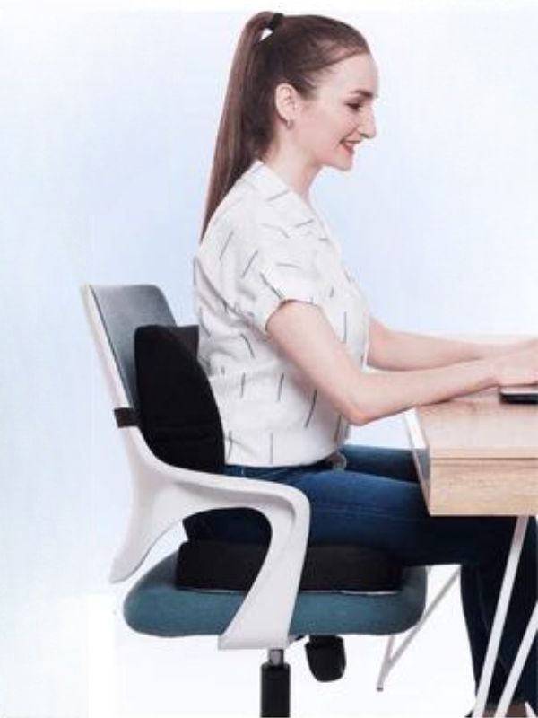 Mulher sentada em uma cadeira com a almofada ortopédica, esticado os braços para cima enquanto tem uma revista aberta no colo.