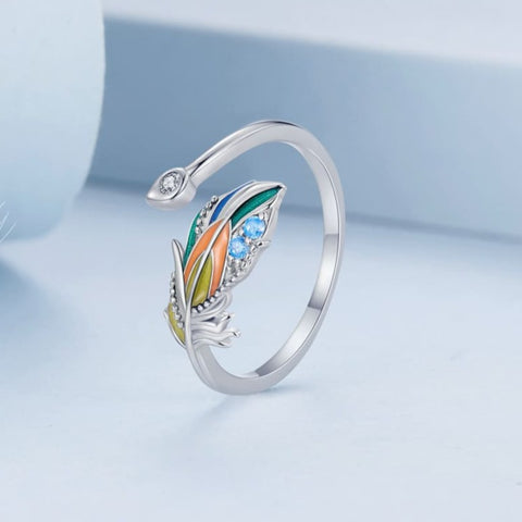 Um anel de prata 925 com uma pena colorida e pedras brilhantes na parte superior, vista frontal.