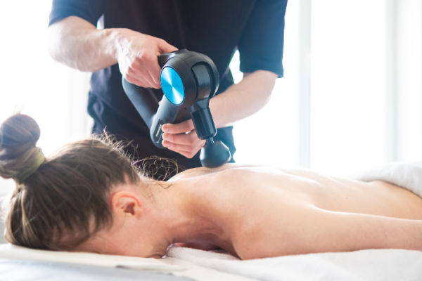 Woman experiencing a back massage with a massage gun