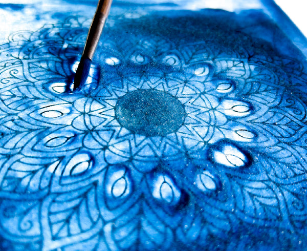 a mandala colored in vibrant blue watercolor atop a light table
