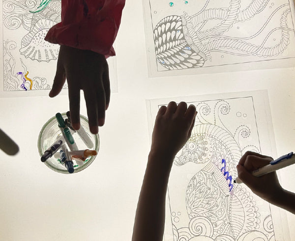 student hands using various mediums to add color to transparencies as they work with a light table in their classroom