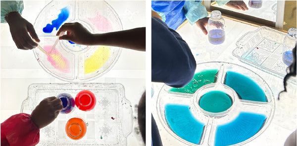 student hands using various mediums including liquid watercolor paint to add color to transparencies as they work with a light table in their classroom