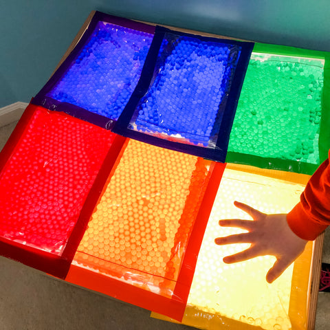 children's hand touching a transparent colored bag on top of a light table