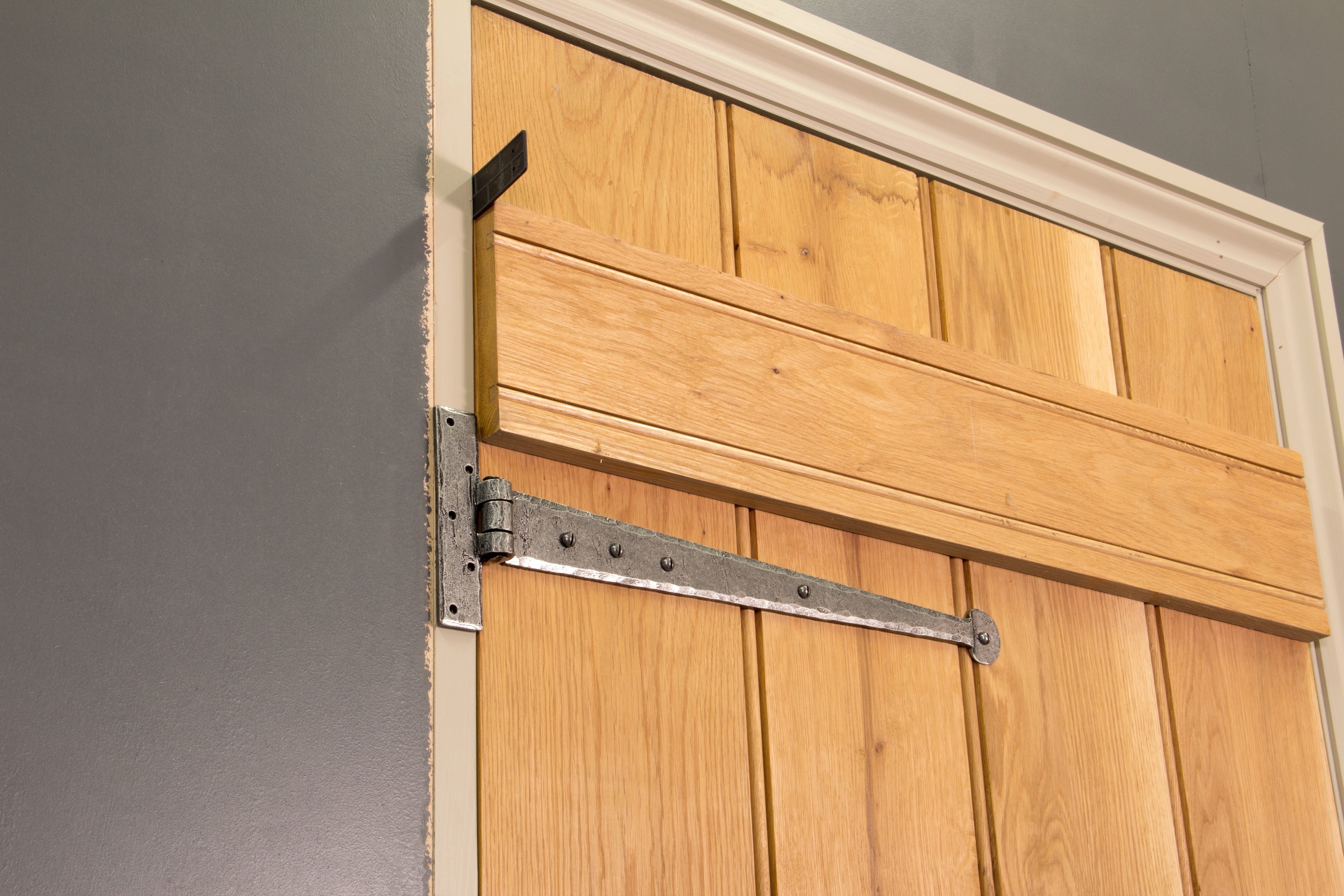 A wooden ledge and brace door hung on a door frame by Pewter Penny End T hinges, with a ruler positioned in the gap as a spacer.