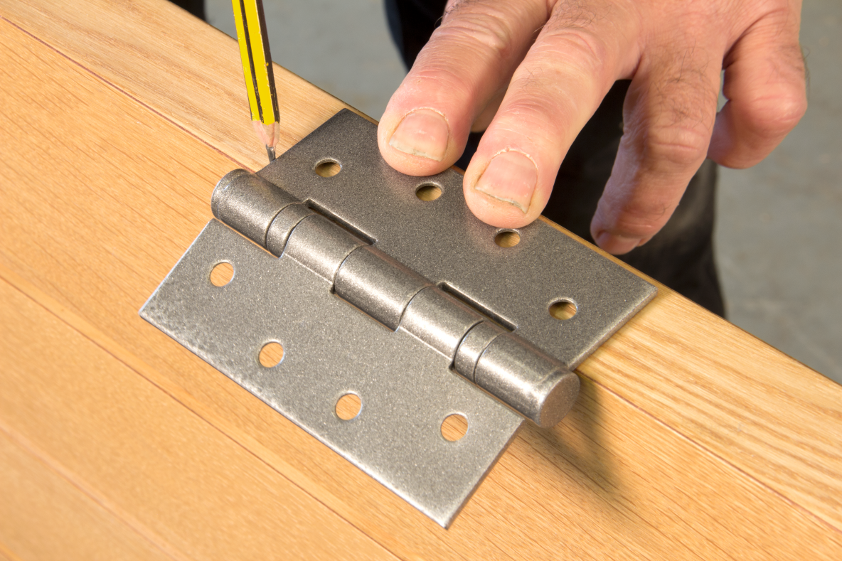 Person marking the position of a Pewter butt hinge on the edge of a wooden door.