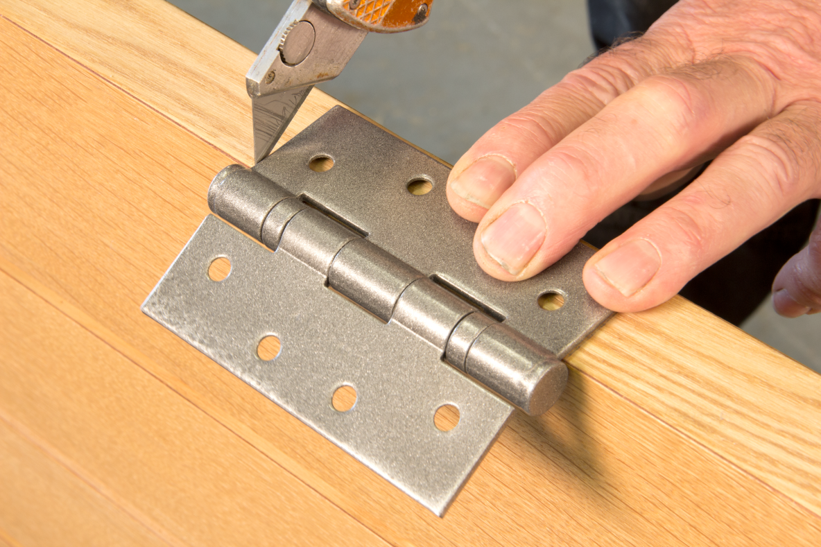 Person using a Stanley blade to score the position of a Pewter butt hinge on the edge of a wooden door.