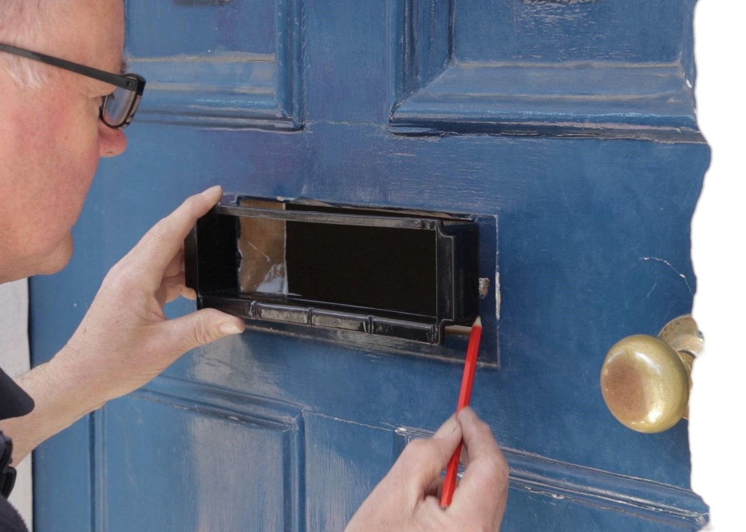 Person using a pencil to mark the position of a letterbox on a blue wooden door.