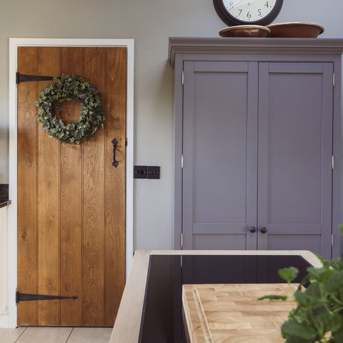 A charming country cottage interior with wood ledge and braced doors with External Beeswax T hinges and thumblatch, next to a grey painted cupboard.