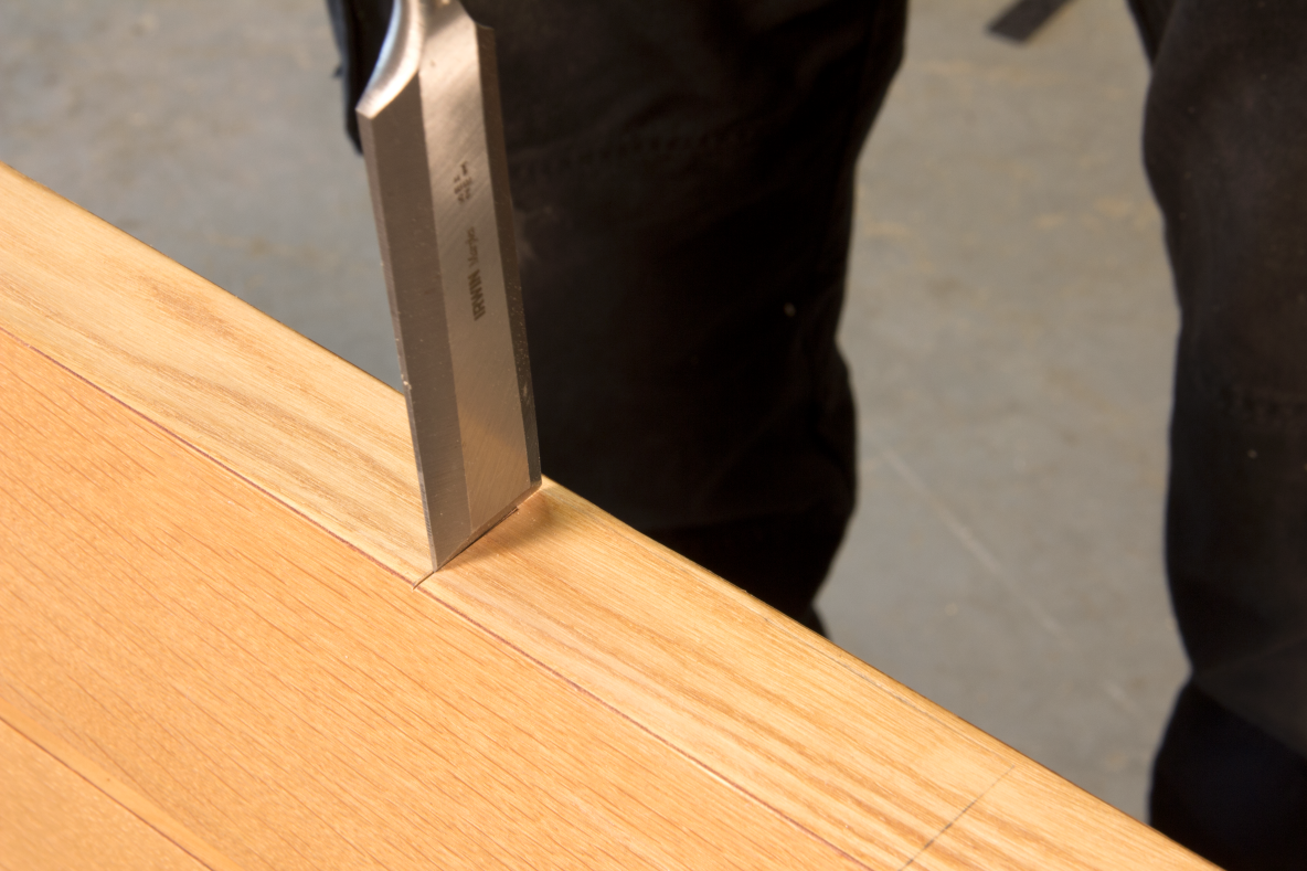 Person using a sharp chisel to chisel out a hole for a hinge in the edge of a wooden door.