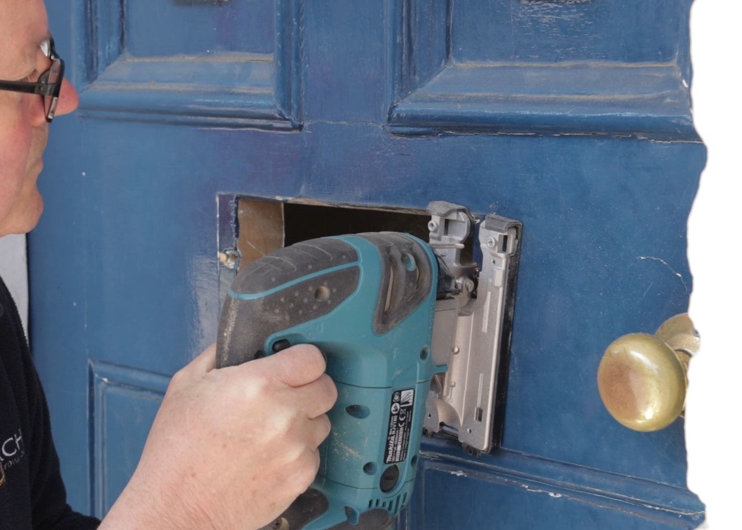 Person using a band saw to cut a hole for a letterbox in a blue wooden door.