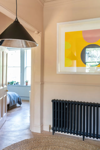 From The Anvil's Hammered Nickel Hockley pendant in a neutral hallway with a black painted radiator and a framed abstract painting hung above it.