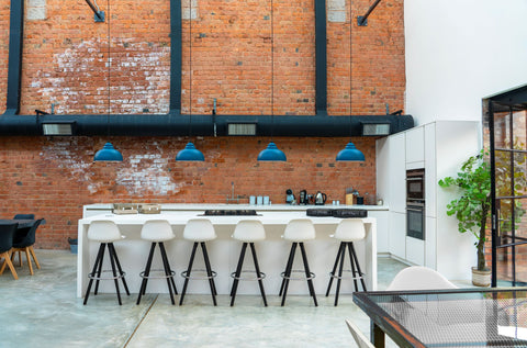 From The Anvil's blue Upstream Hammered Nickel Brindley ceiling pendants in a row over a white marble ktichen against a red brick wall.