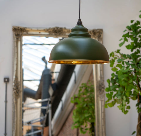 From The Anvil's Hammered Brass Brindley pendant with a dark green Heath exterior, hung from the ceiling above a staircase, in front of an ornate gold framed mirror.