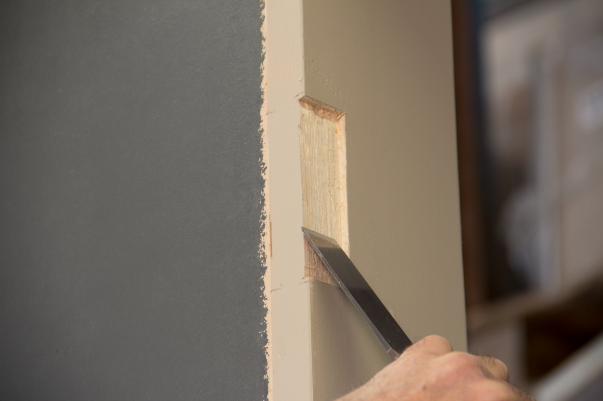 Person using a sharp chisel to chisel out a space in a wooden door frame for a butt hinge