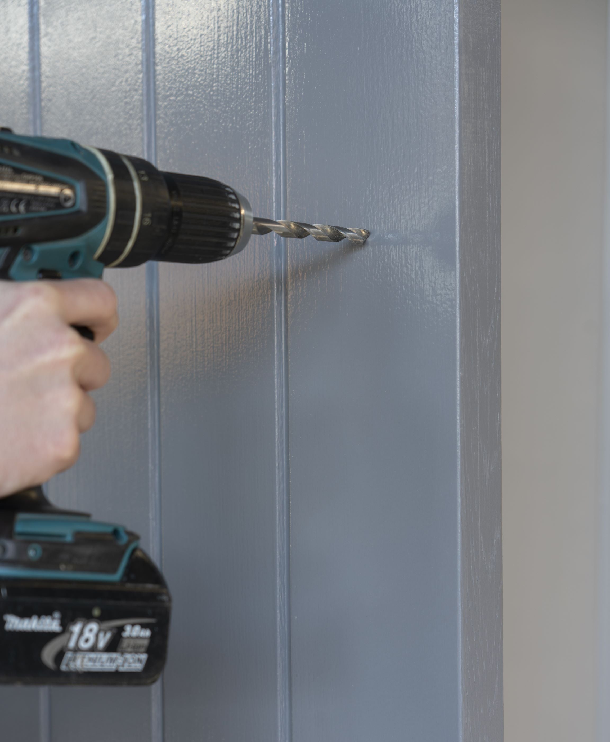 Person using an electric drill to drill holes in a grey panelled door.