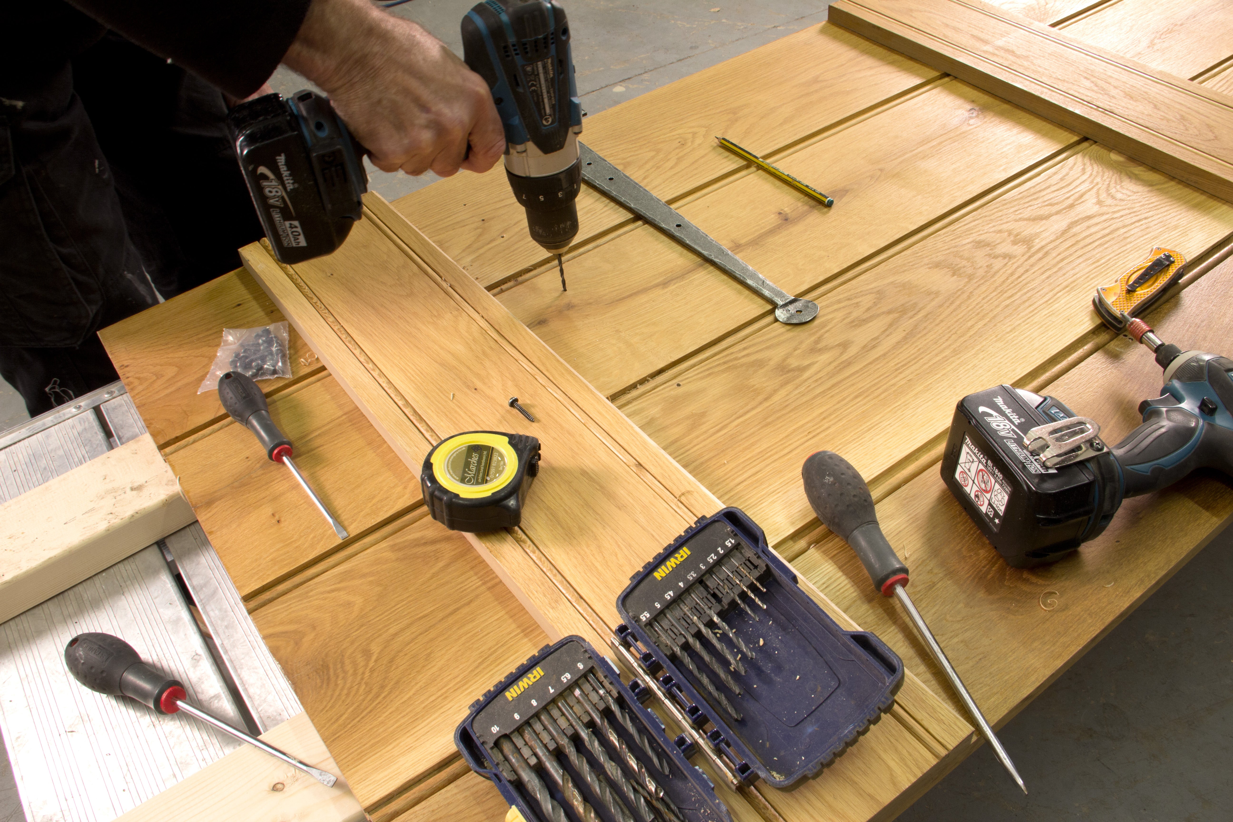 Person using an electric drill to drill pilot holes in the position of screw holes on a wooden ledge and brace door.