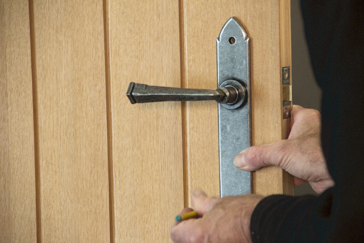 Person marking the fixing holes of a Pewter lever door handle on a wooden door.