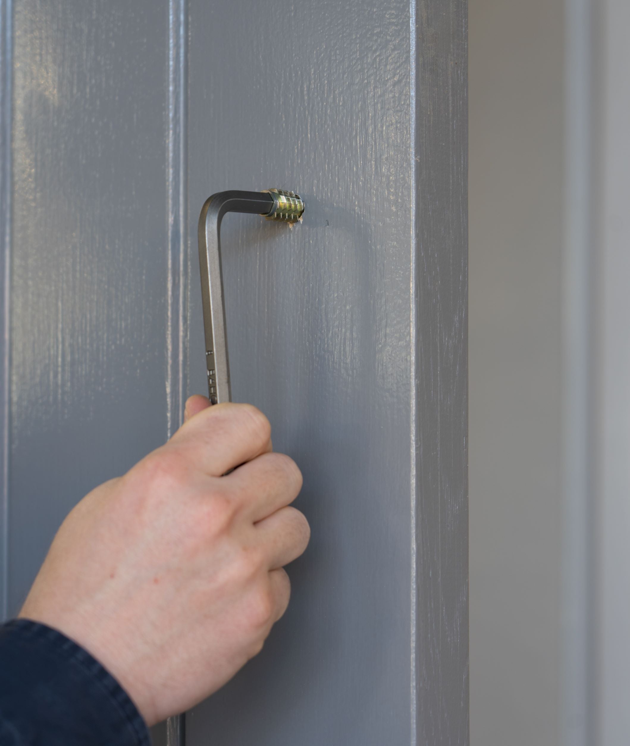 Person using an Allen key to tighten a grommet into a grey pannelled door.