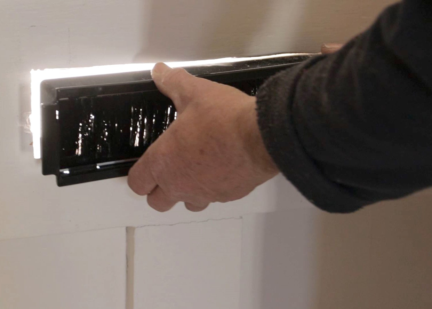 Person inserting the brush section of a traditional letterbox to the interior side of the door.