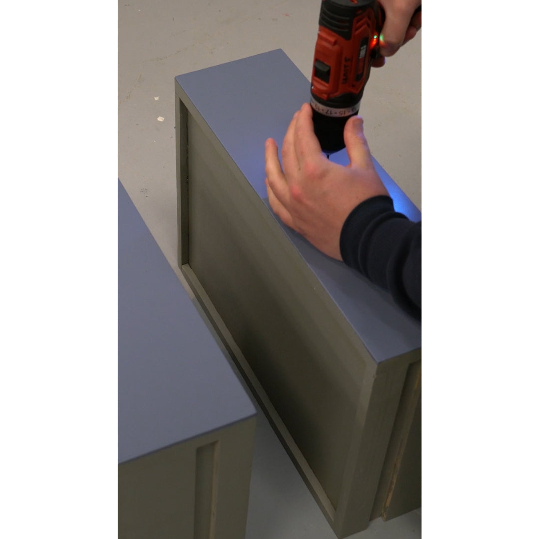 Person using an electric drill to drill a hole in a chest of drawers for a cabinet knob.
