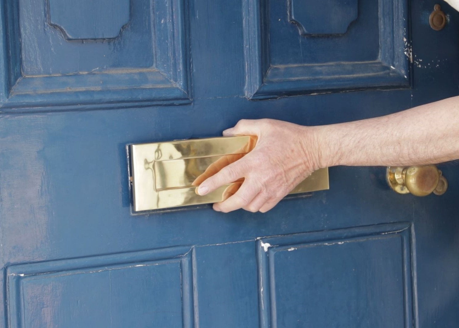 Person fitting the front of a brass letterbox to a blue wooden door.