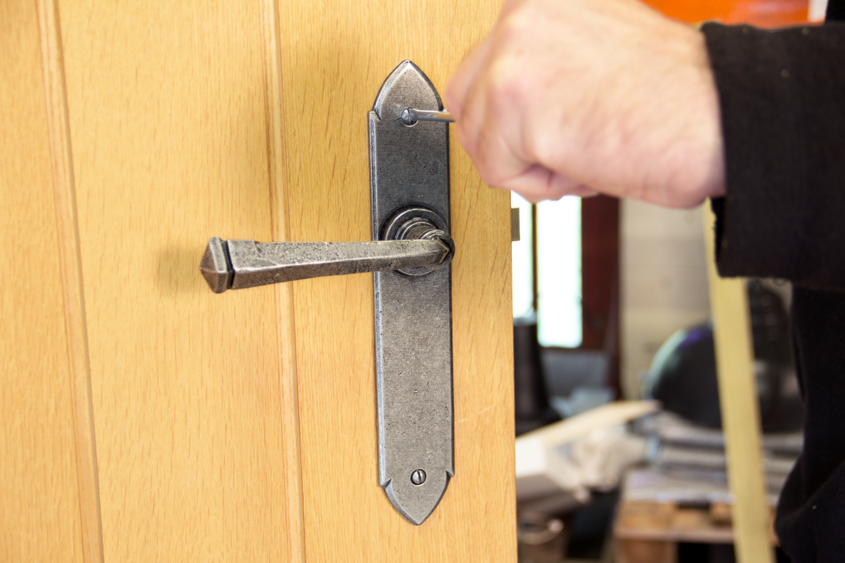 Person using a screw driver to fit a Pewter door handle to a wooden door