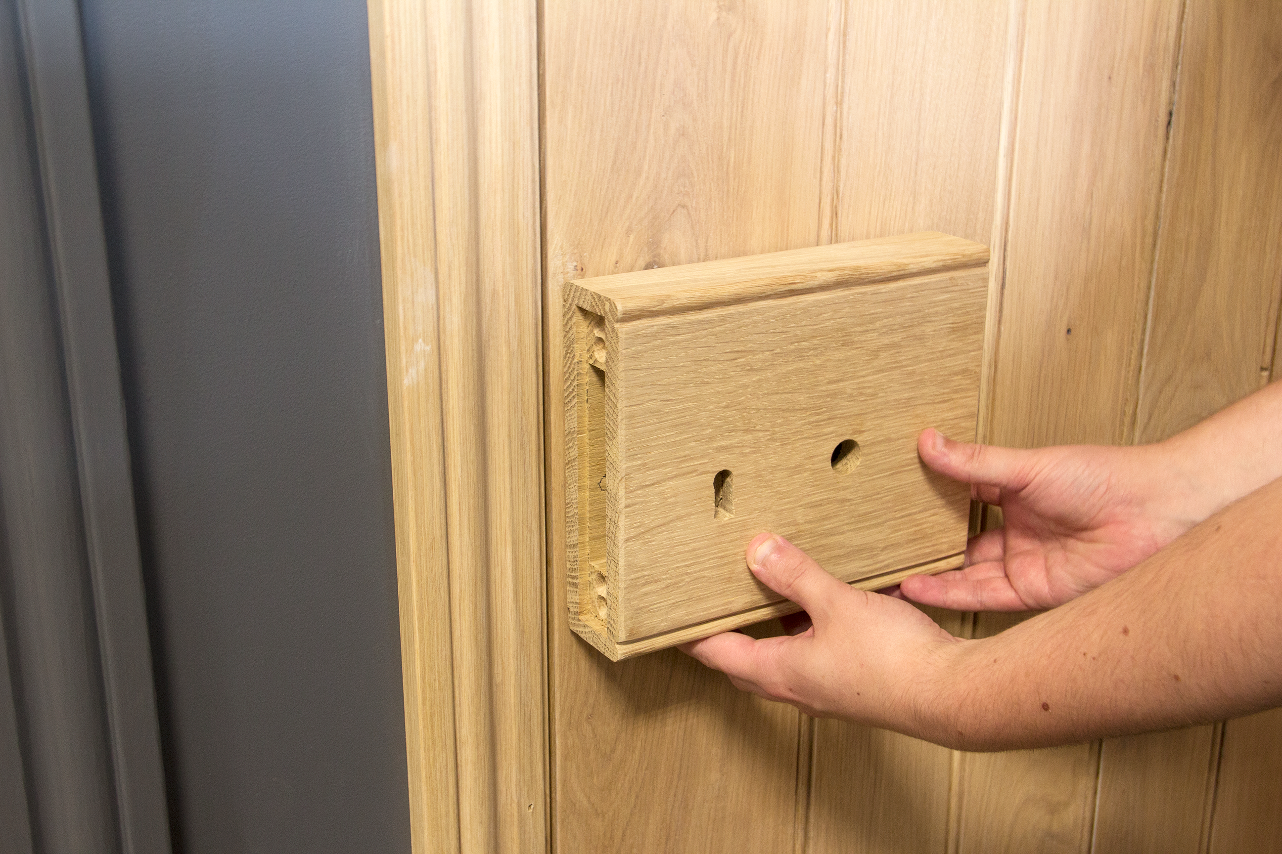 Person holding an oak box lock against a wooden door,
