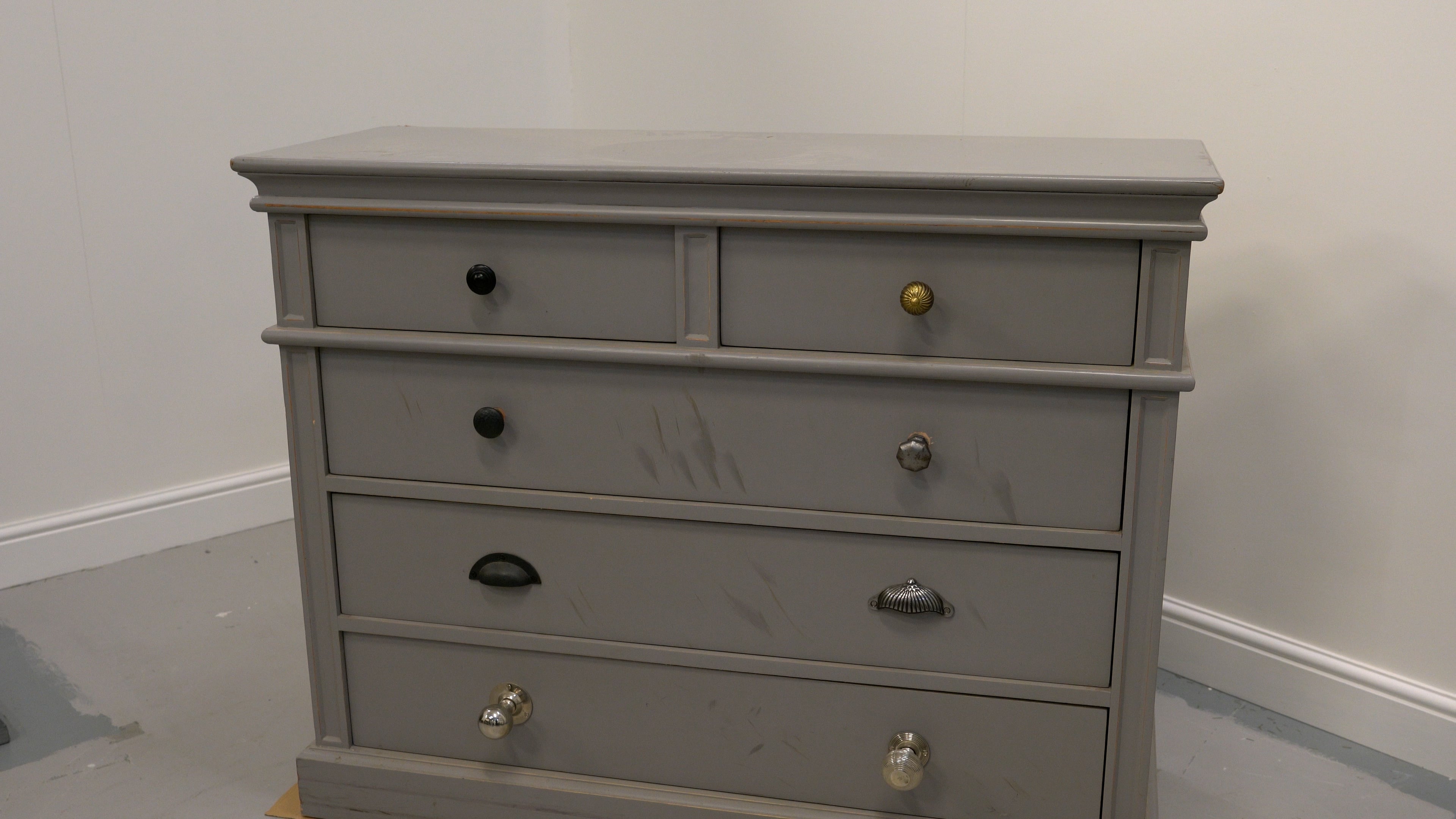 An old, battered chest of draws with mis-matched hardware and lots of scratches.