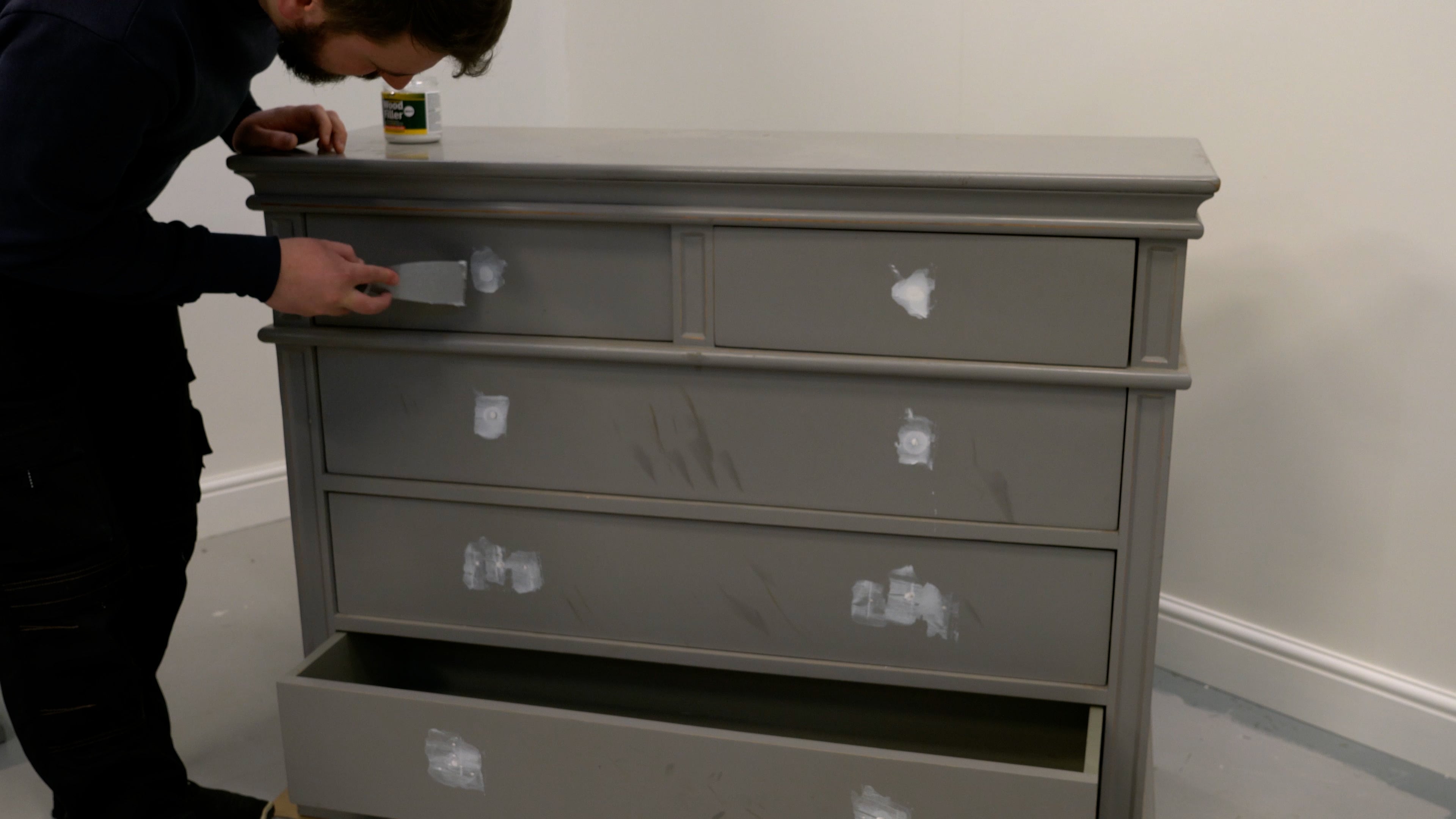 Person using wood filler and a scraper to fill holes in a wooden chest of drawers.