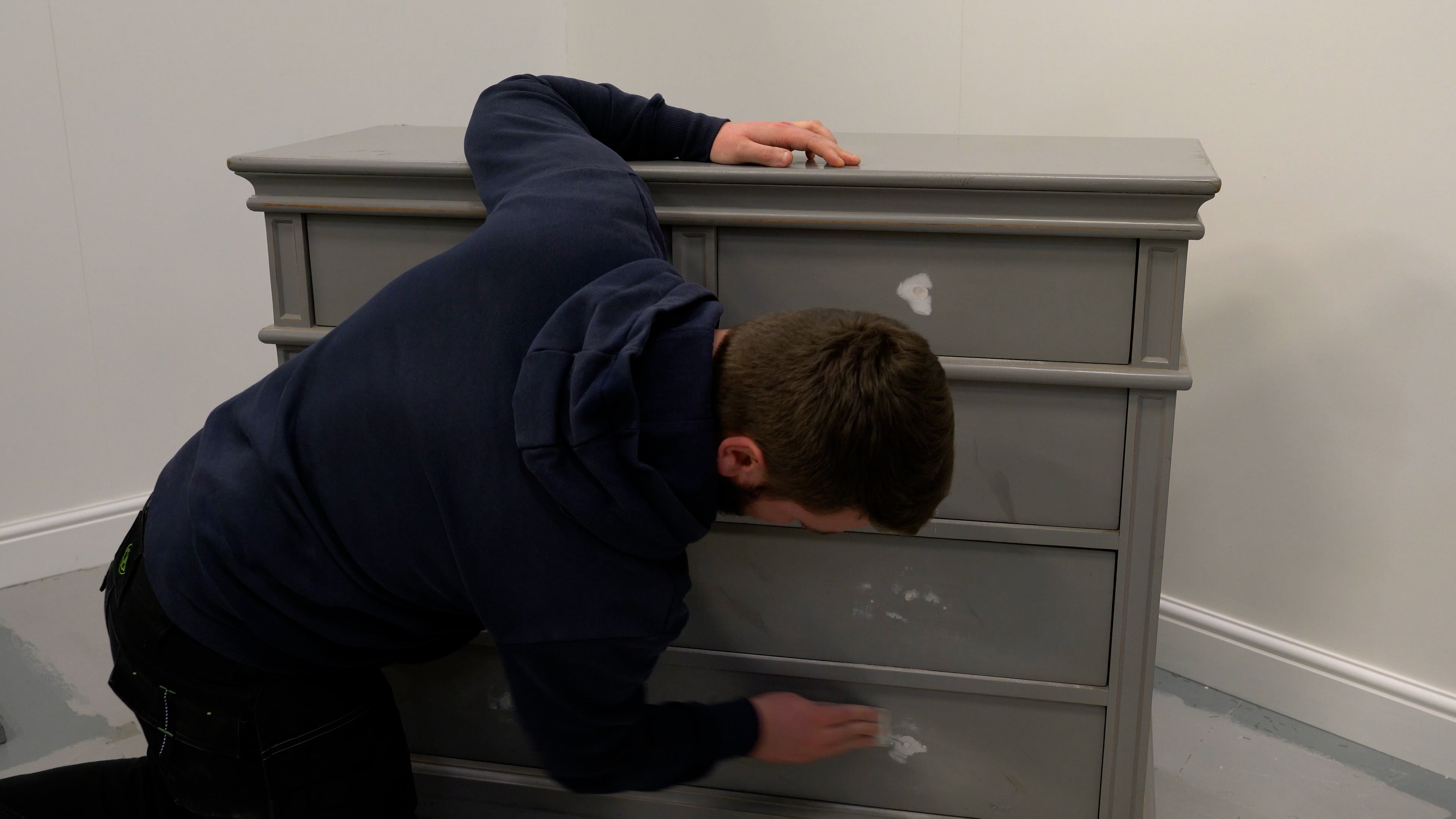 Person using sand paper to smoothen the surface of an old chest of drawers.