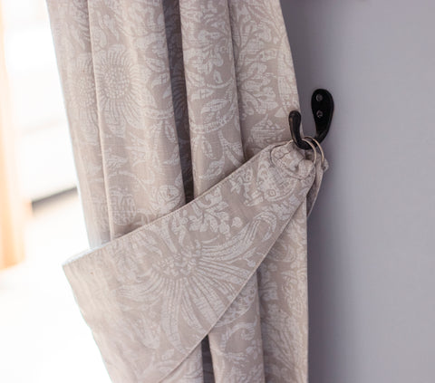From The Anvil's Black Robe hooks being used as a curtain tieback for a pair of patterned curtains against a neutral wall.