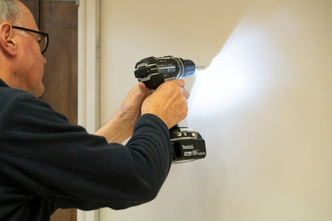 Man holding a Makita drill against a white wall drilling a hole.