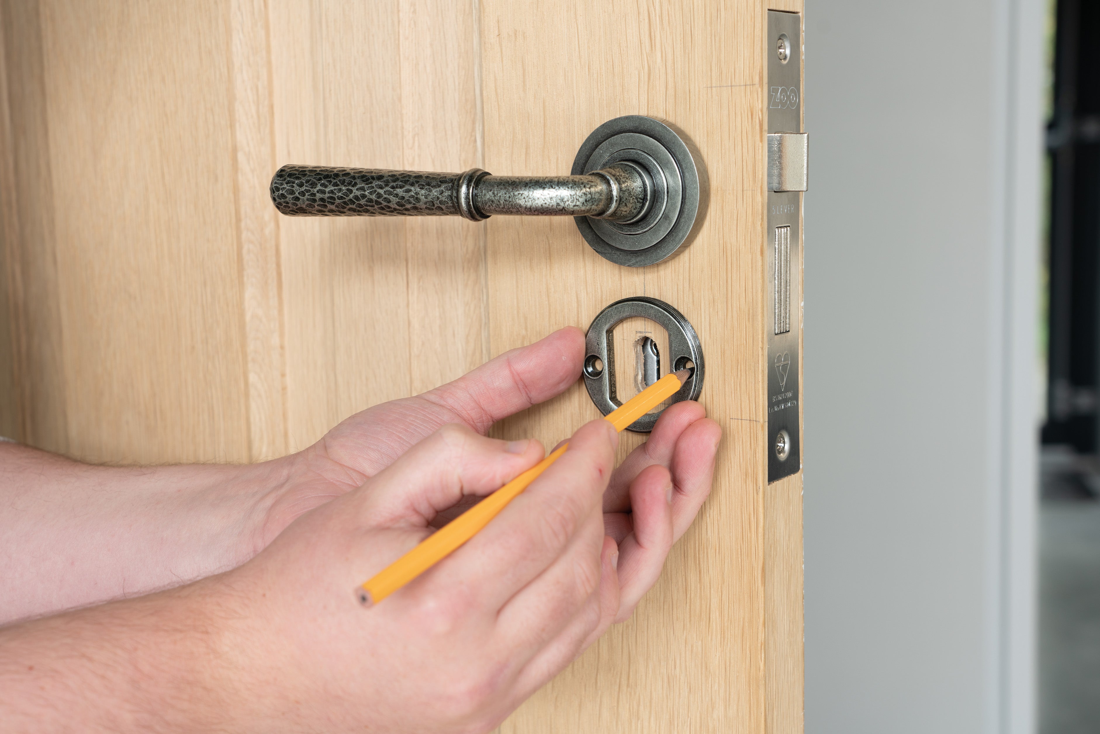 Person using a pencil to mark the position of the screw holes on a Pewter concealed escutcheon on a wooden door, underneath a Pewter lever on rose door handle.