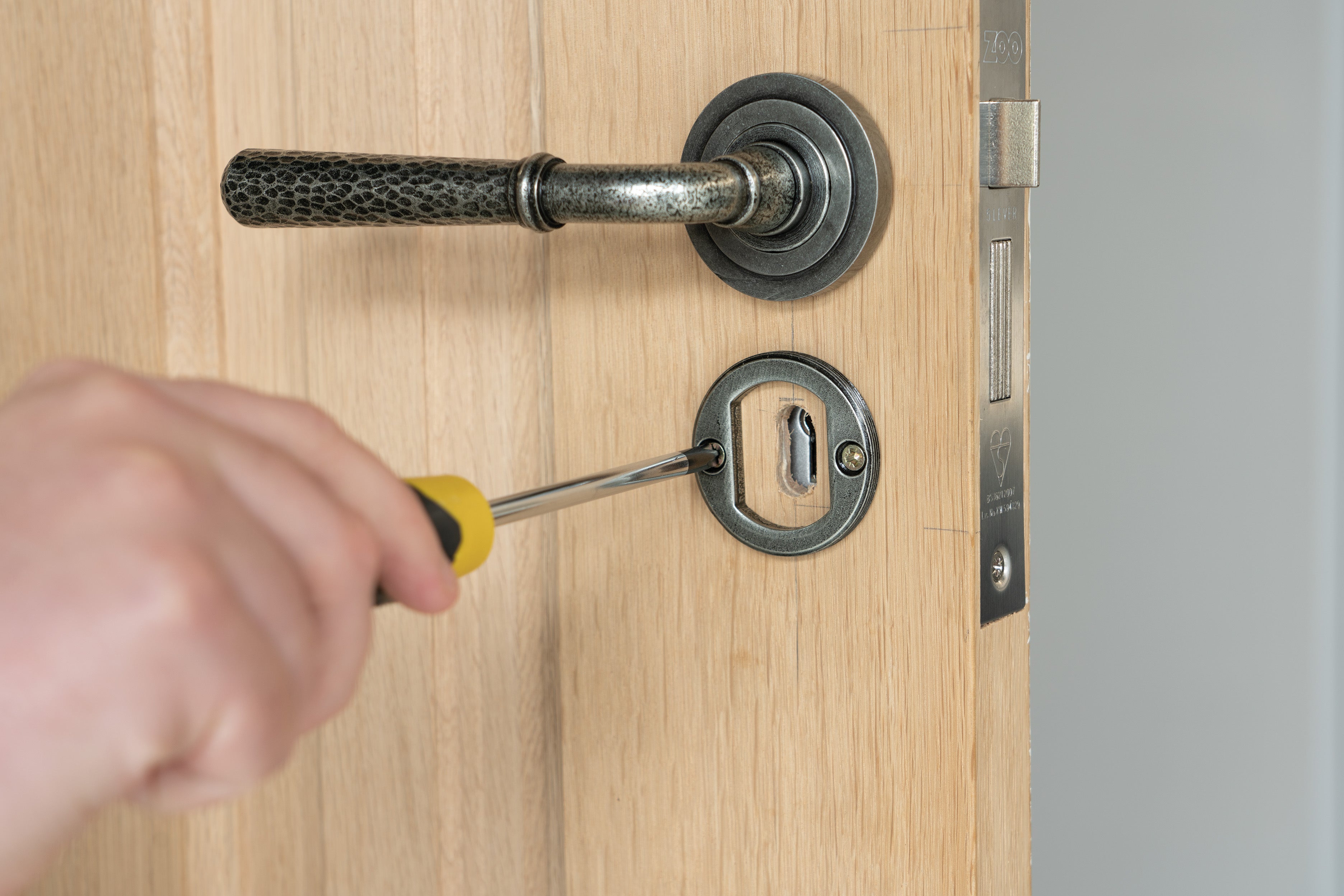 Person using a screwdriver to tighten the screws in a concealed Pewter escutcheon on a wooden door.