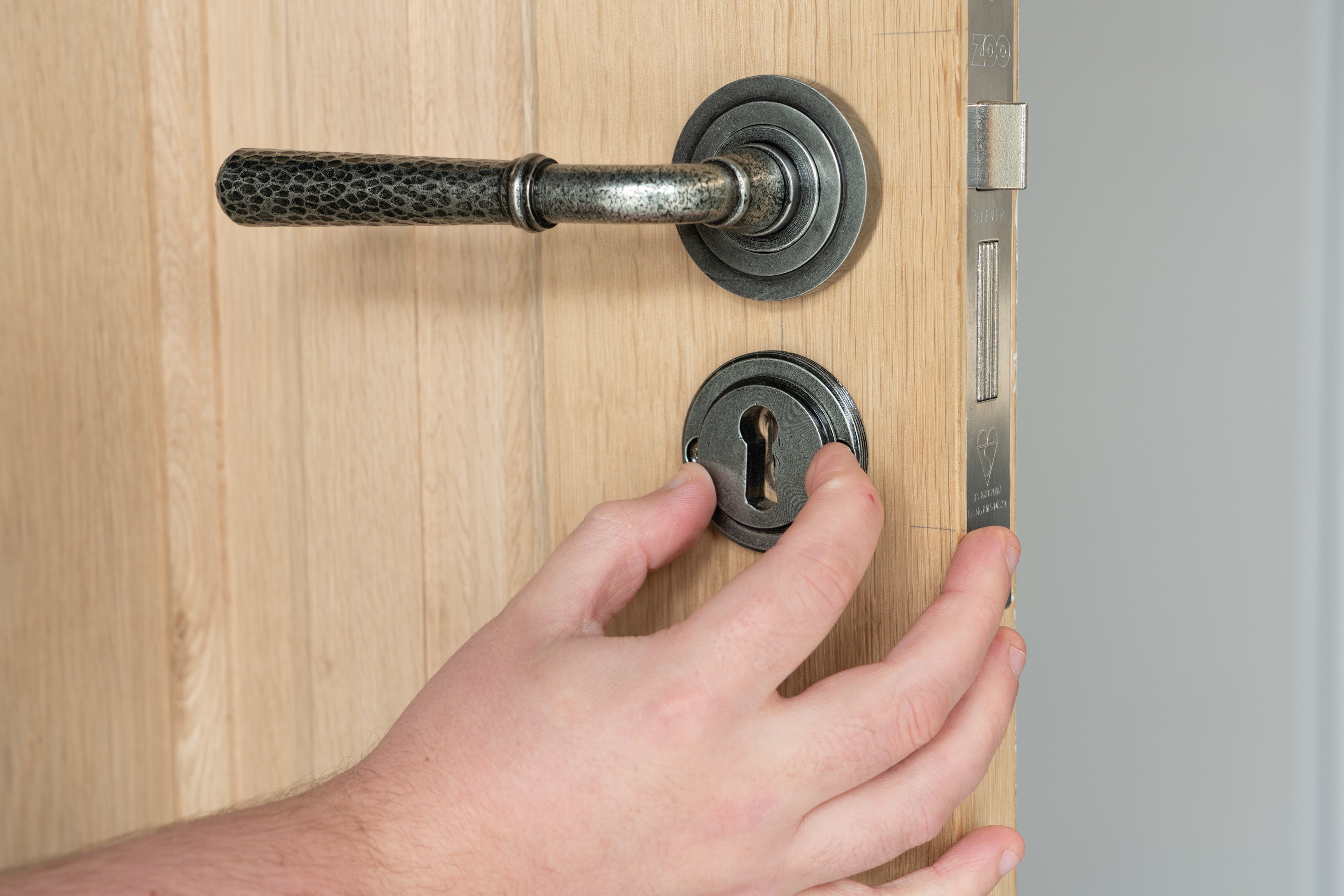 Person tightening a round rose onto a concealed escutcheon on a wooden door.