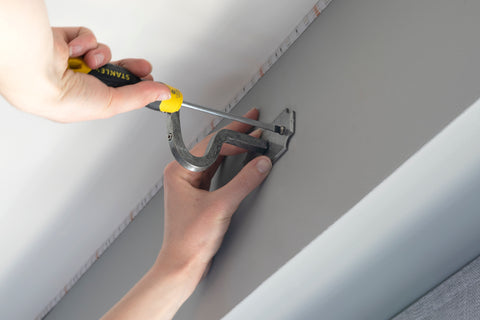 Person using a screw driver to fit a Pewter mounting bracket to a wall above a window