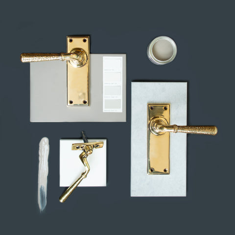 A moodboard of From The Anvil's Hammered Brass door handles and window espag. handles on grey and slate tiles, on a dark navy blue background.