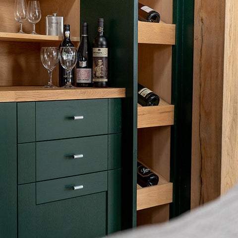 From The Anvil's Judd T-bar pull handles on a dark green painted set of drawers with wooden shelving & countertop, with wine glasses and drink bottles on top.