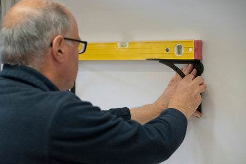 Man using a spirit level to determine the levelness of a From The Anvil shelf bracket.