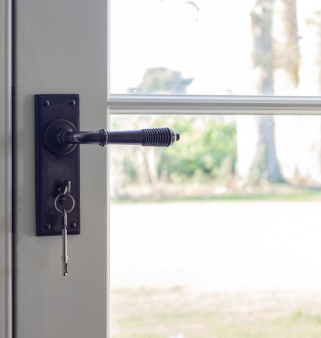 From The Anvil's Aged Bronze Reeded lever lock door handle set with a key in it on a painted door frame with windows.