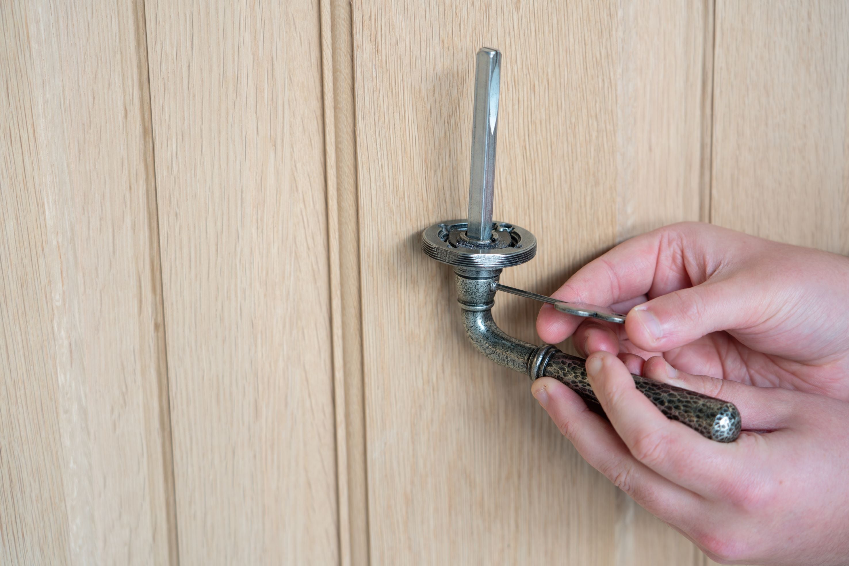 Person tightening the grub screw on a Pewter lever on rose door handle, using an Allen key.