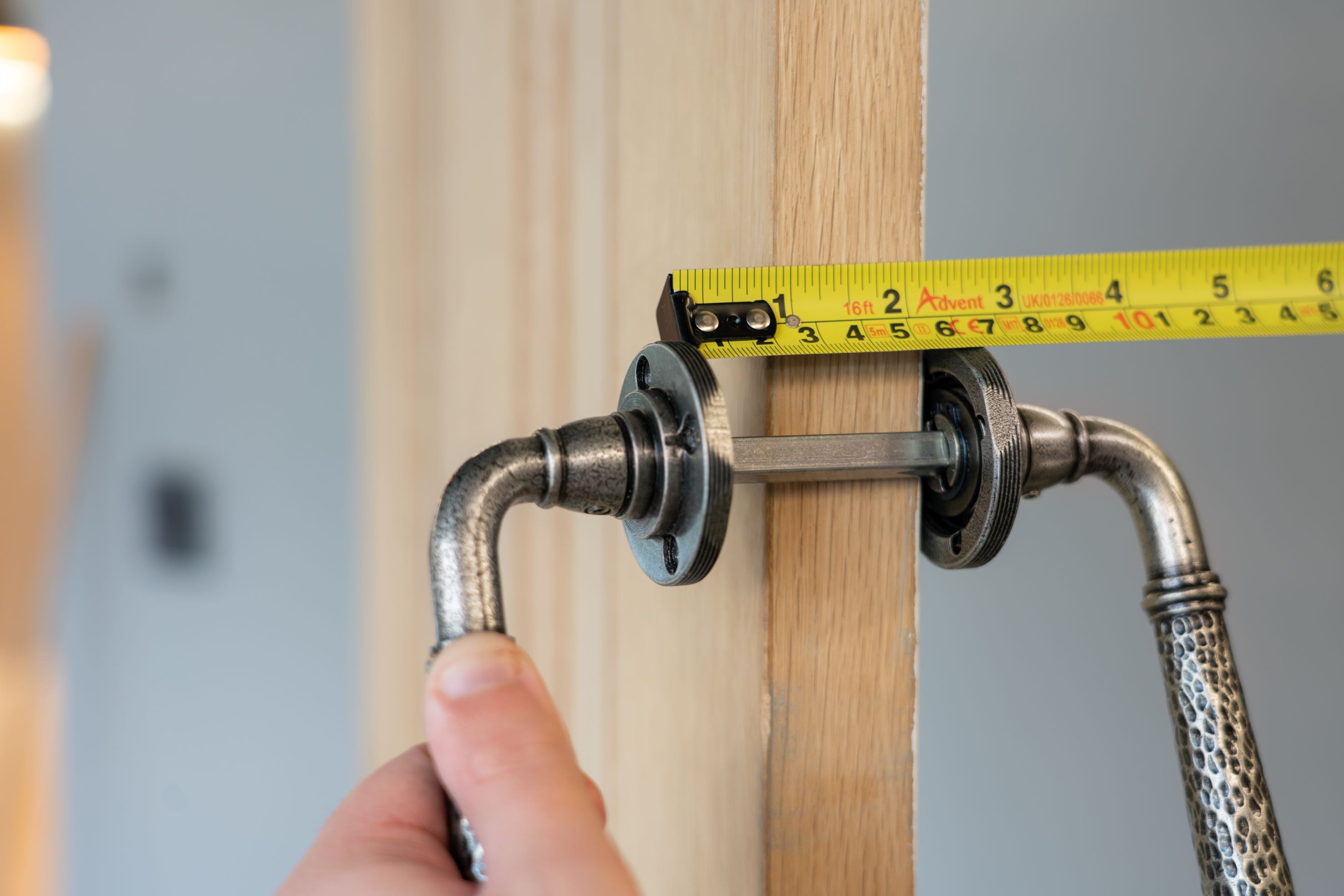 Person using a measuring tape to measure the excess length of a spindle passing through a wooden door.