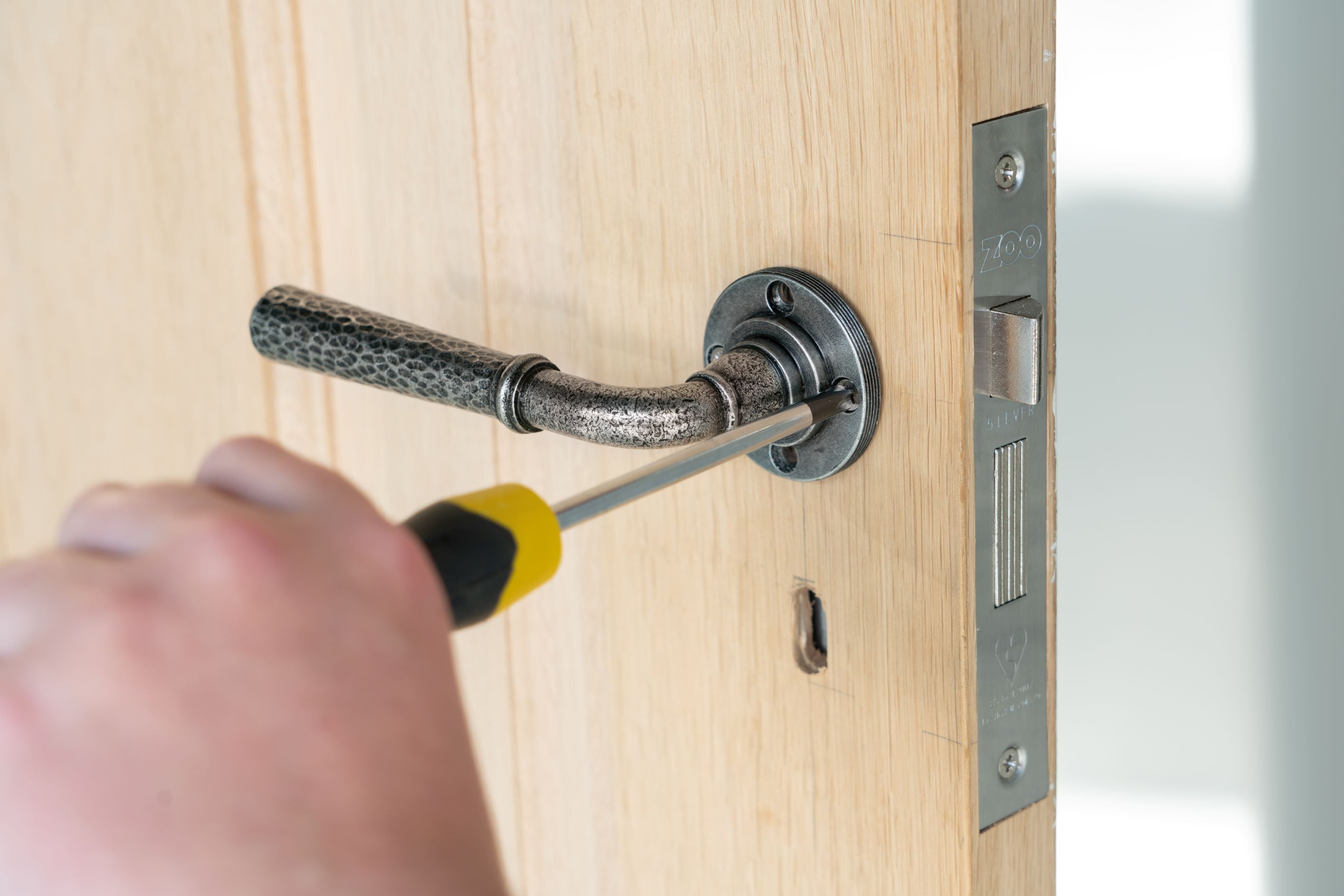 Person using a screw driver to tighten the screws on a lever on rose door handle fitted to a wooden door.
